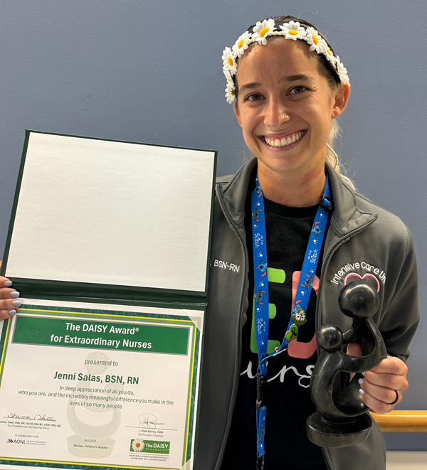 awardee wearing a headband of daisies, daisy award statue, and certificate.