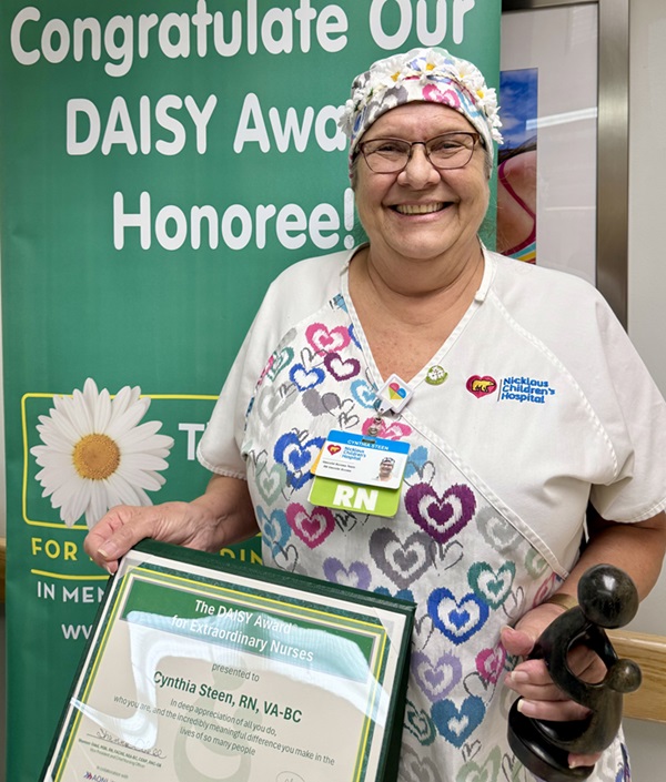 awardee wearing a headband of daisies, daisy award statue, and certificate.