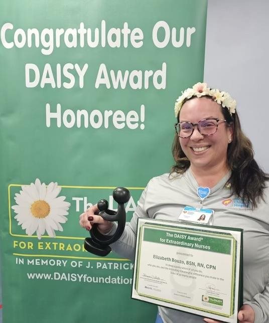 awardee wearing a headband of daisies, daisy award statue, and certificate.